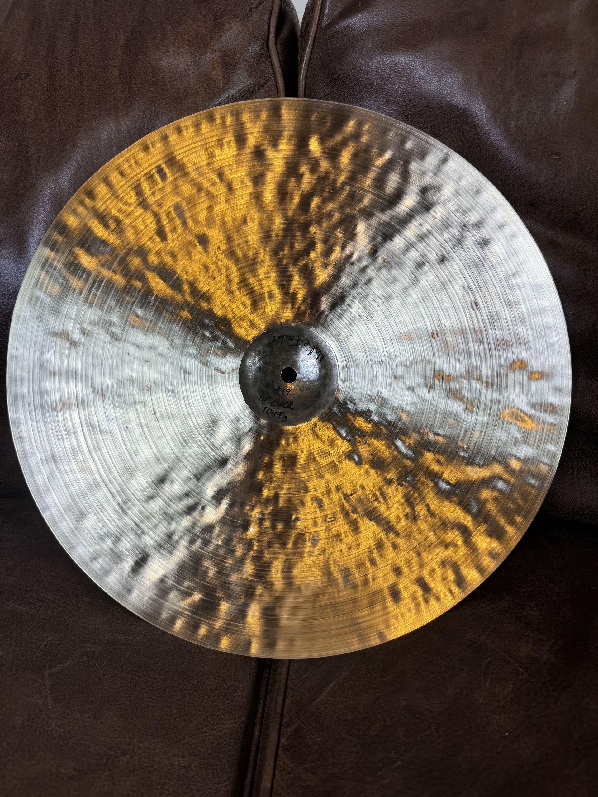 Dark bronze cymbal with a yellow-gold center, resting on a brown leather surface.