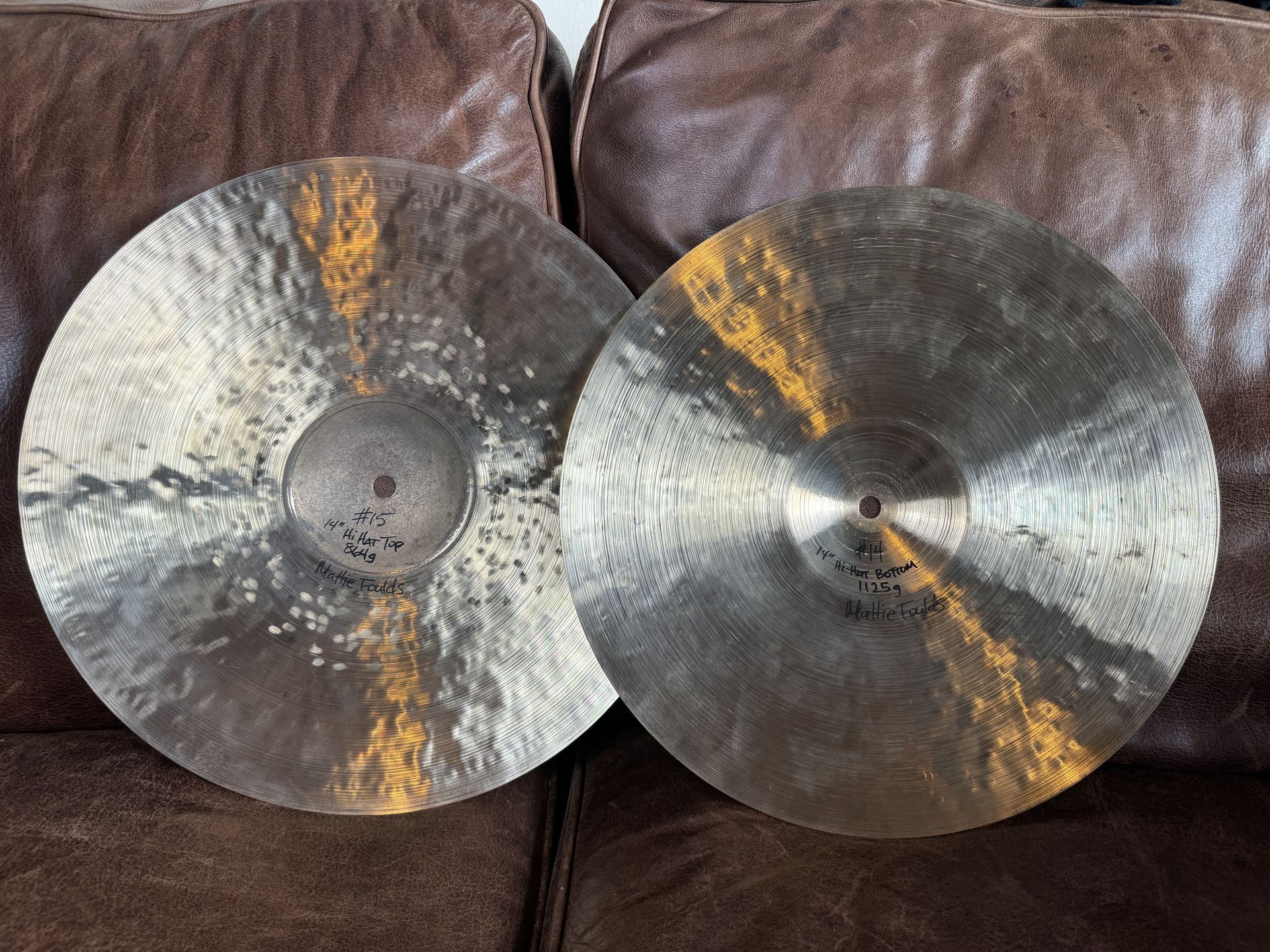Two bronze cymbals on a brown surface. One has more texture than the other.