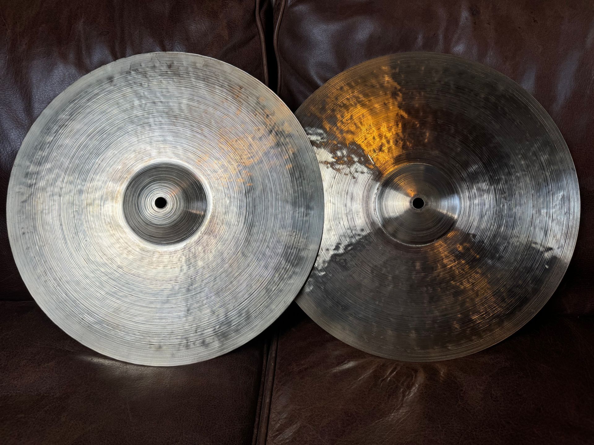Two bronze cymbals, one lighter, the other darker, on a brown surface.