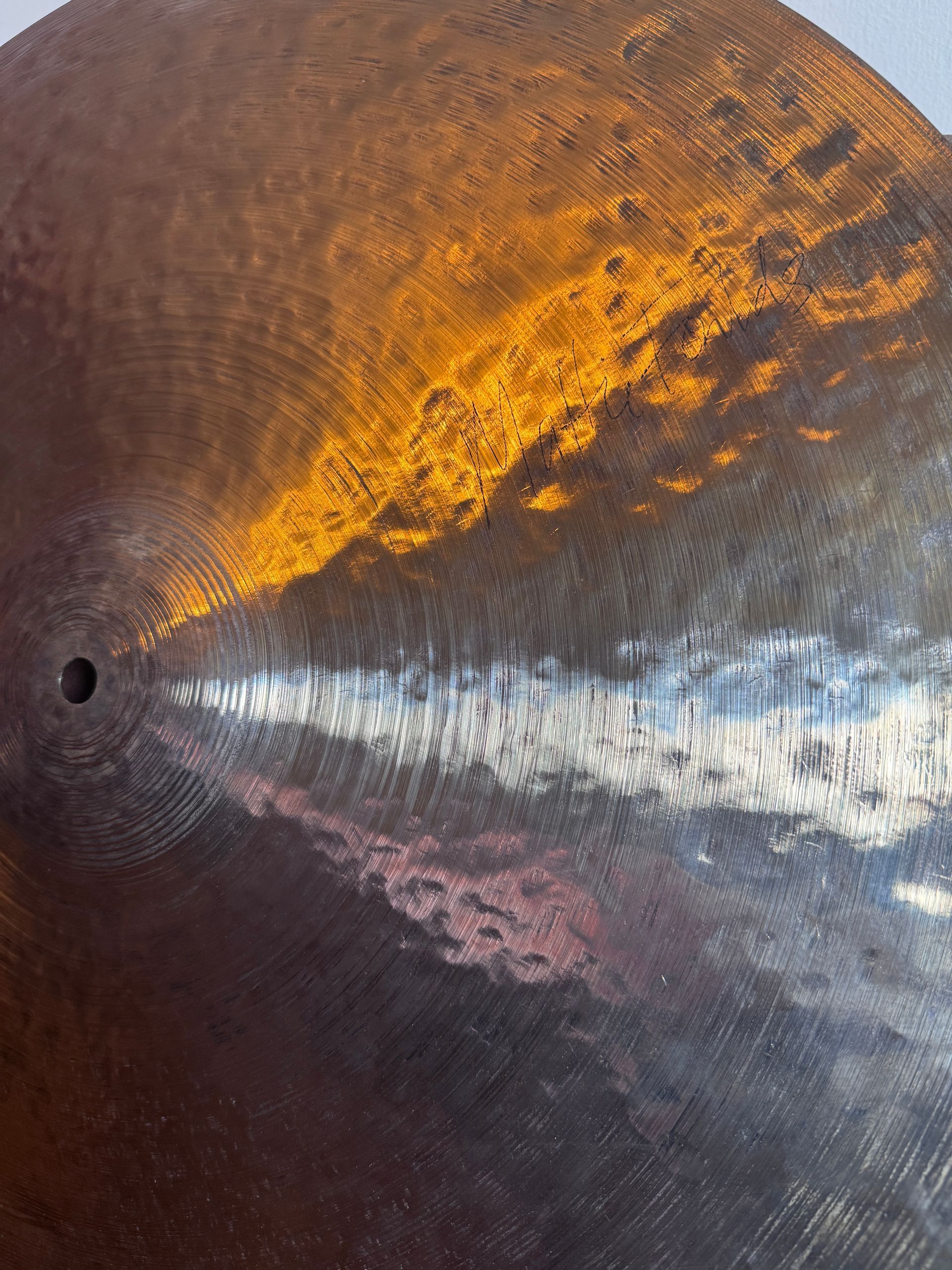 Close-up of a circular metal surface with a small hole. Light reflects, creating gold and silver hues.