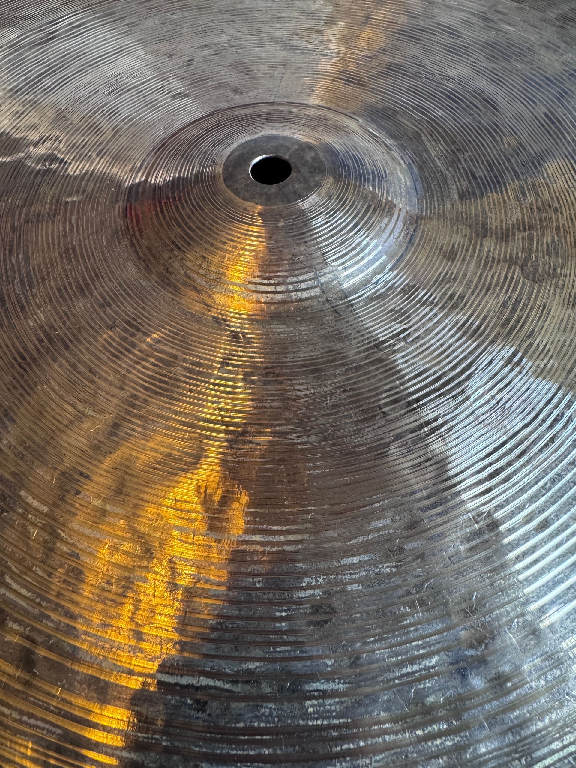 Close-up of a cymbal with concentric circular grooves, a central hole, and a light reflection.