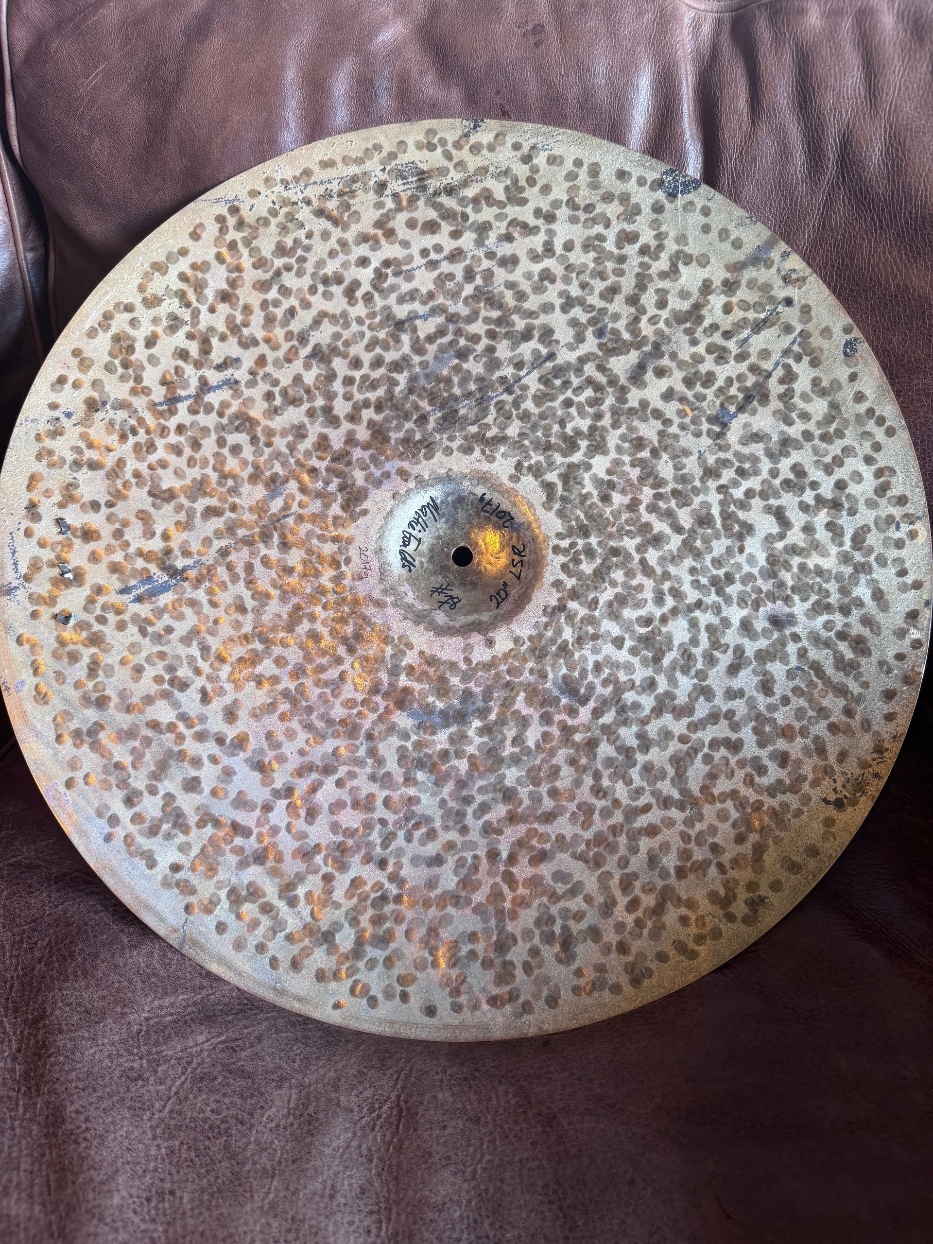 A heavily textured, tarnished cymbal with a central hole, resting on a brown surface.
