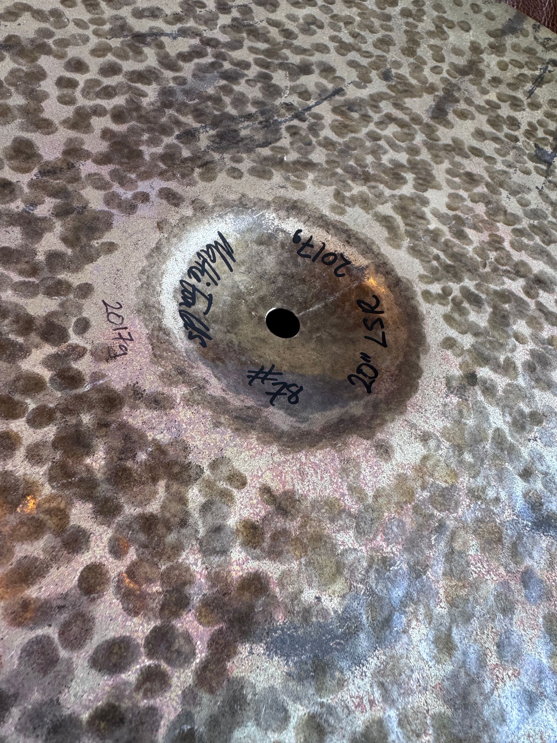 Close-up of a dark cymbal with ink markings around the center hole; appears worn and aged.