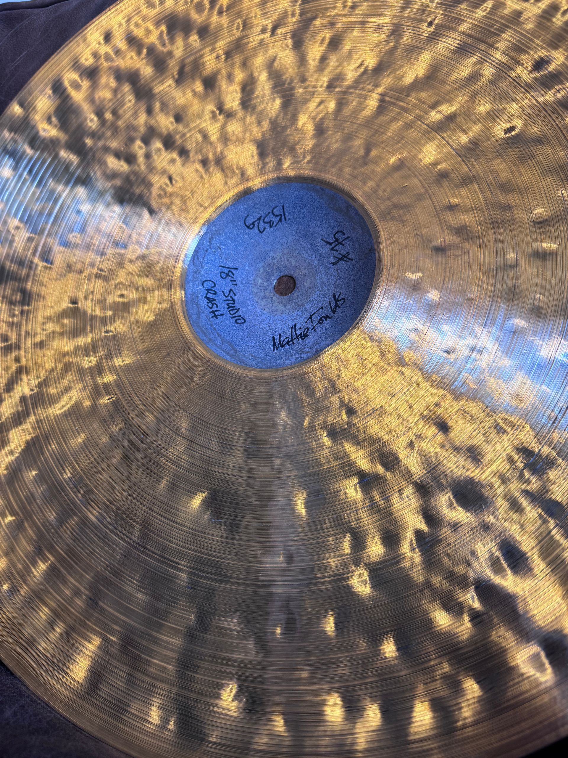 Close-up of a bronze-colored cymbal with a blue center signed by a musician.