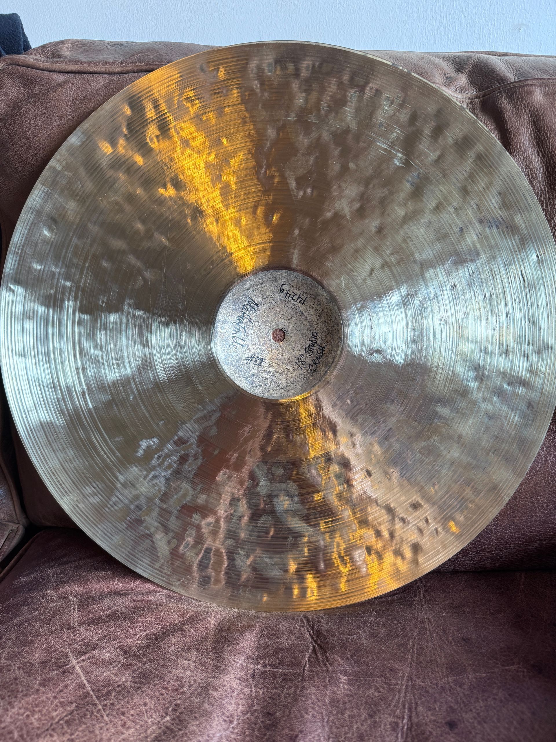 Bronze cymbal with a central hole, resting on a brown surface.