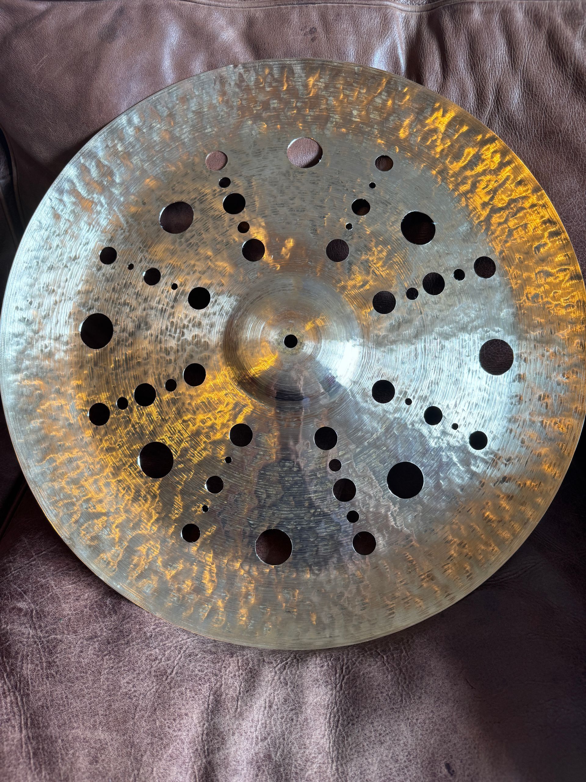 A bronze cymbal with many holes, lying on a brown surface.