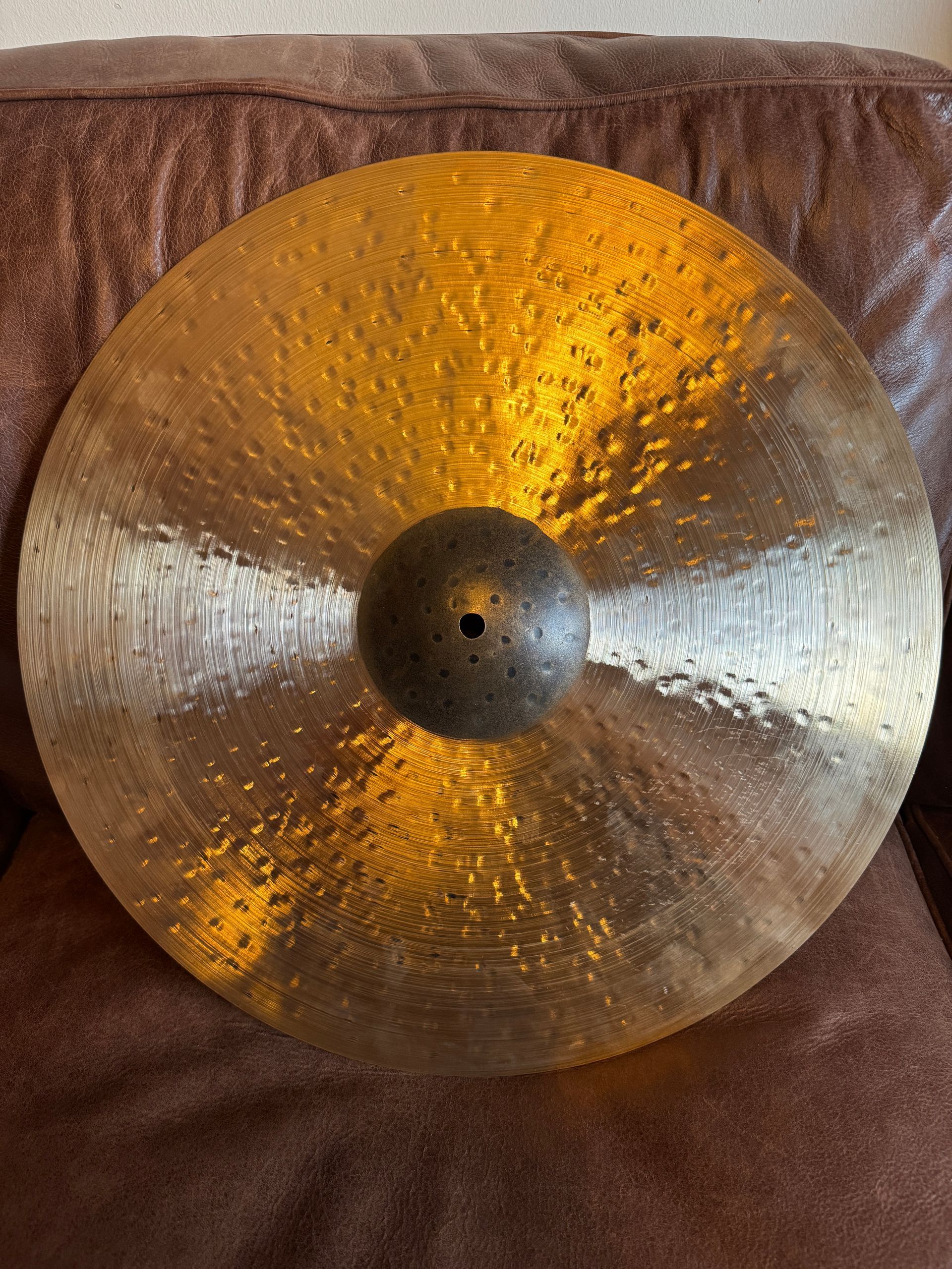 A bronze-colored cymbal with a textured surface, resting on a brown surface.