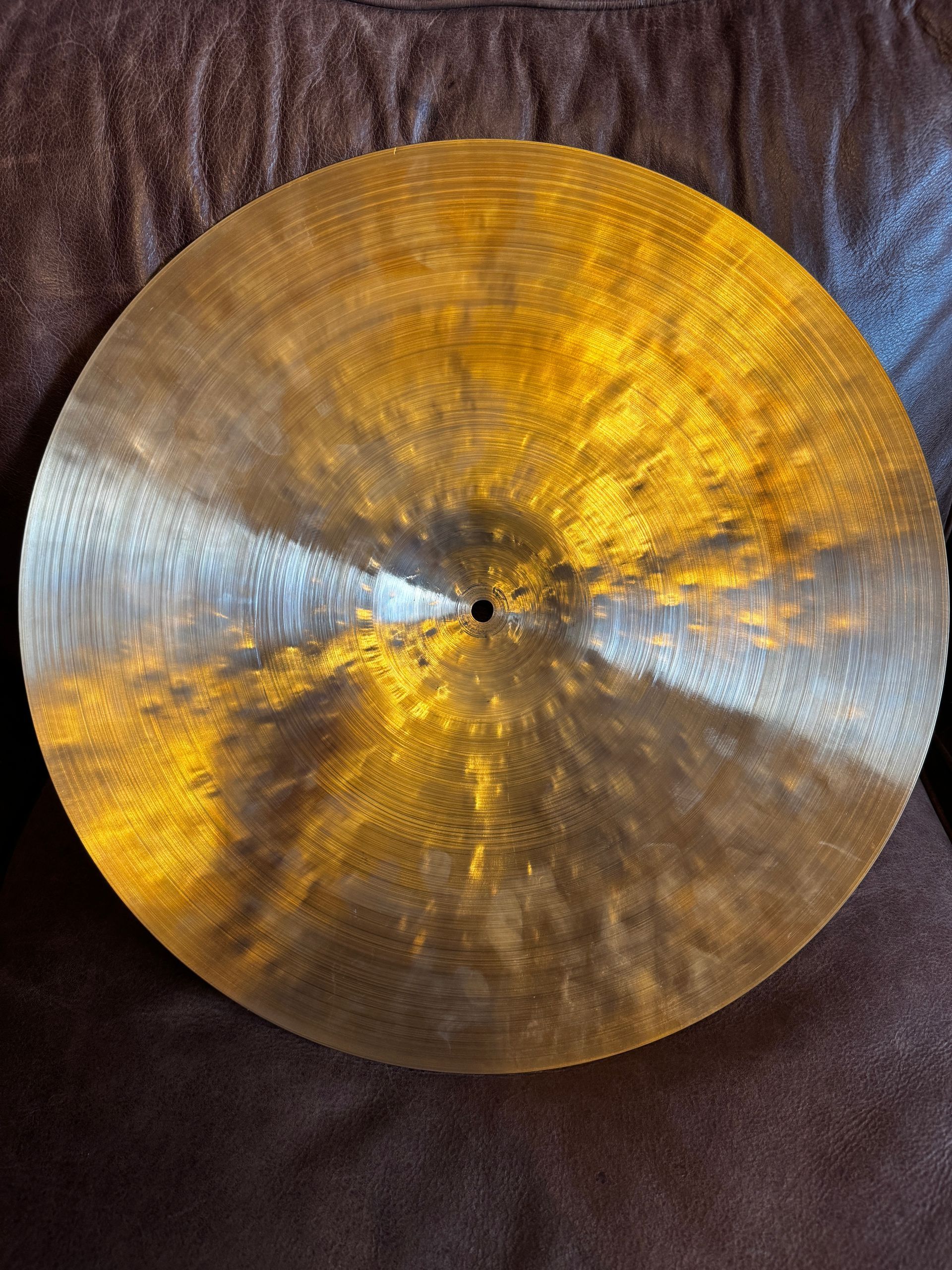 A bronze-colored cymbal with a textured surface, resting on a brown surface.