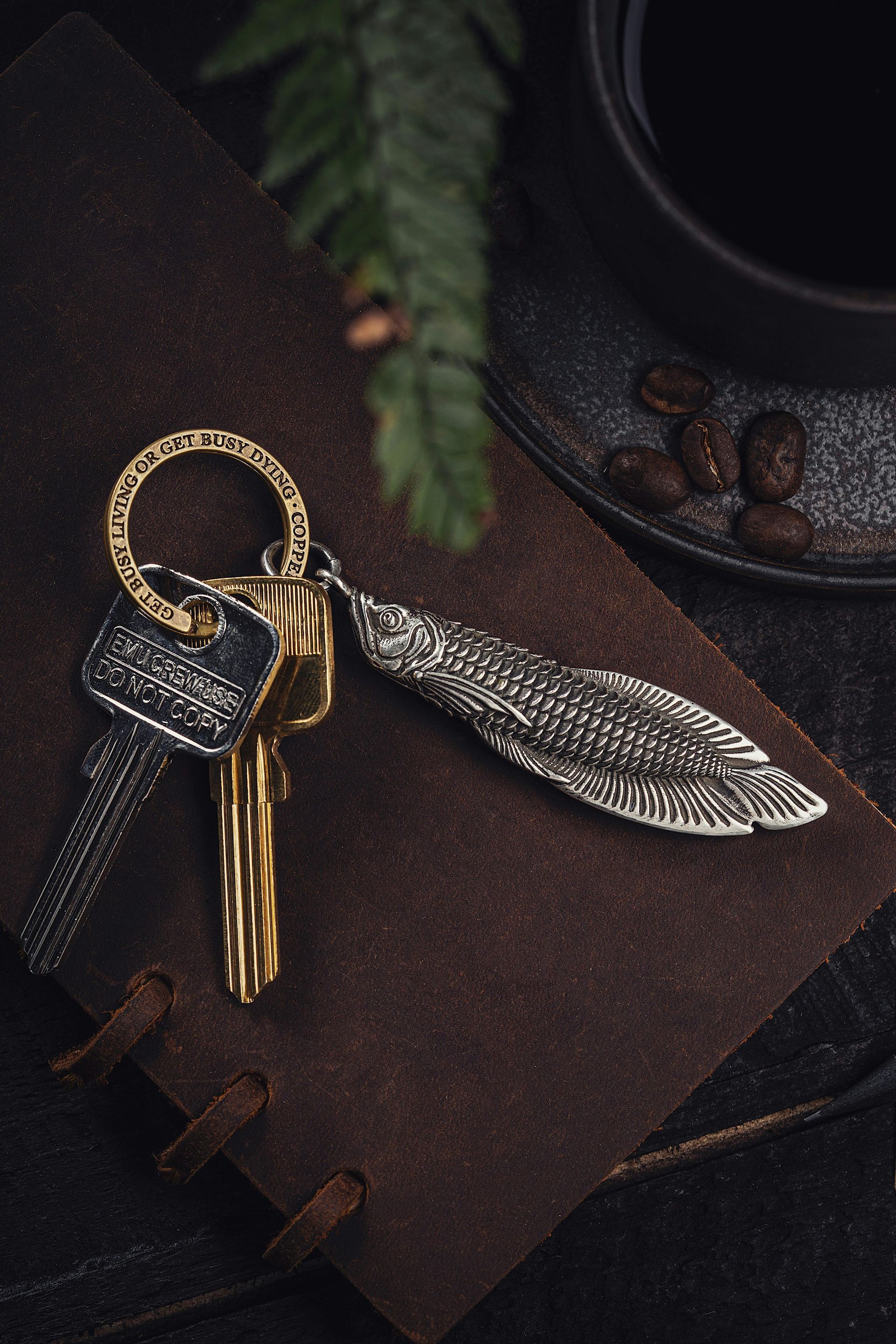 Keys on a leather notebook with a feather-shaped keychain next to a cup of coffee.