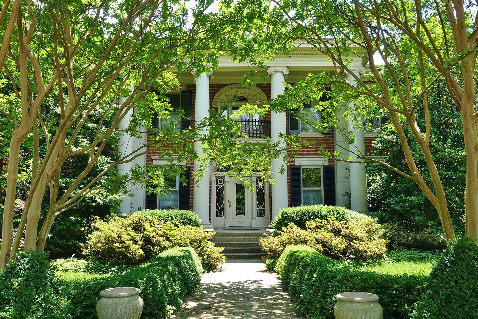 A large white house is surrounded by trees and bushes