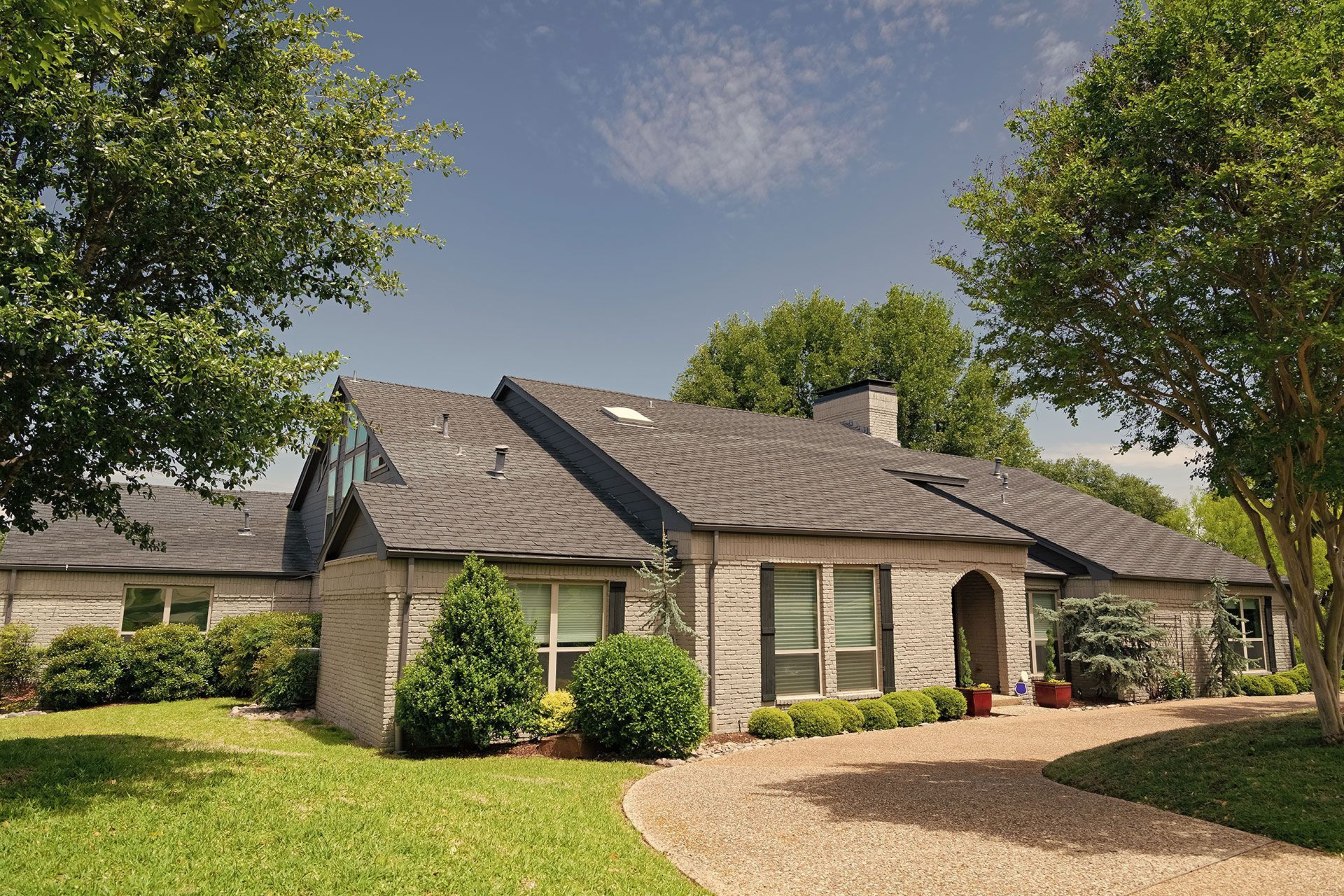 A brick house with a gravel driveway and trees in front of it.