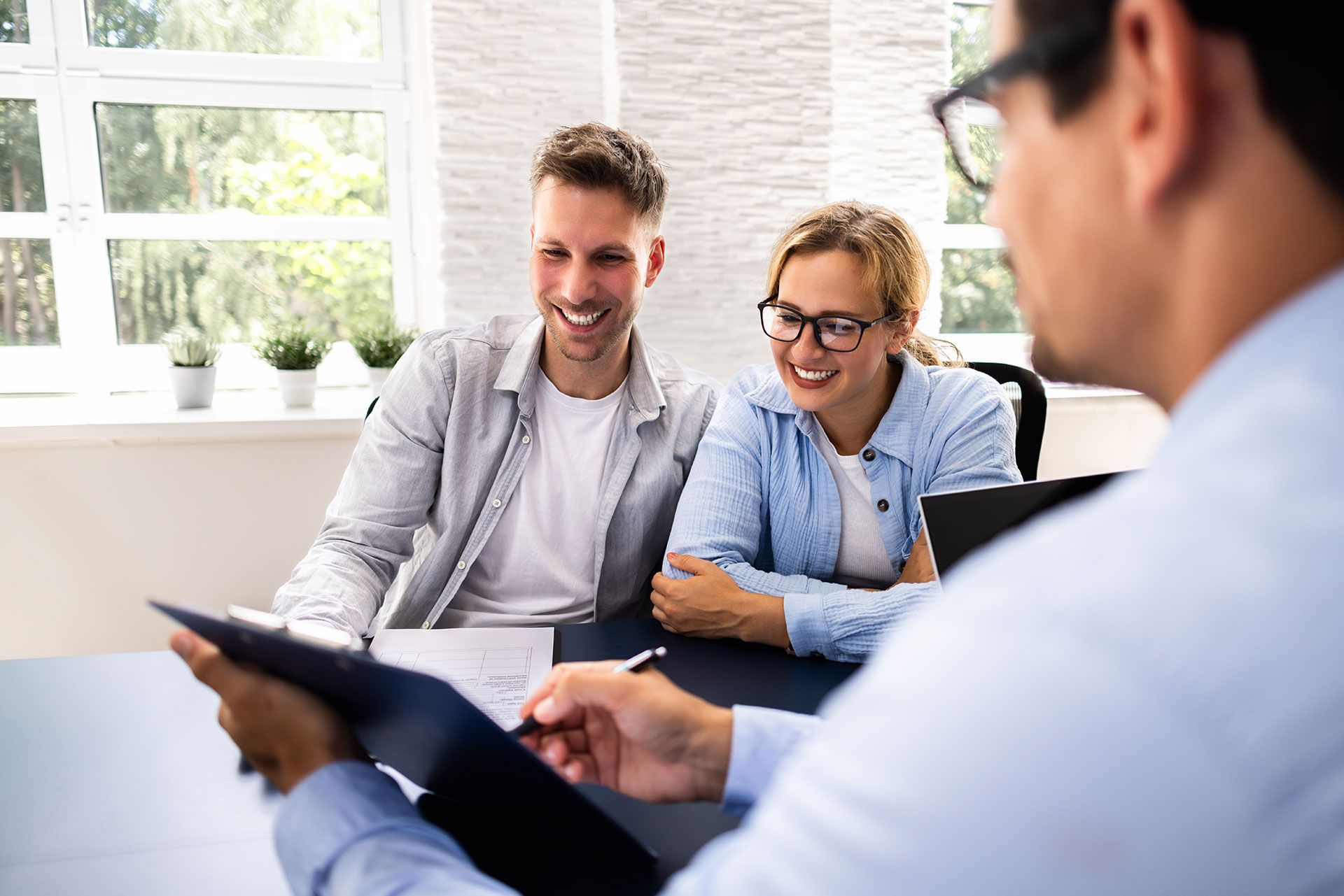 A man is holding a clipboard in front of a couple sitting at a table.