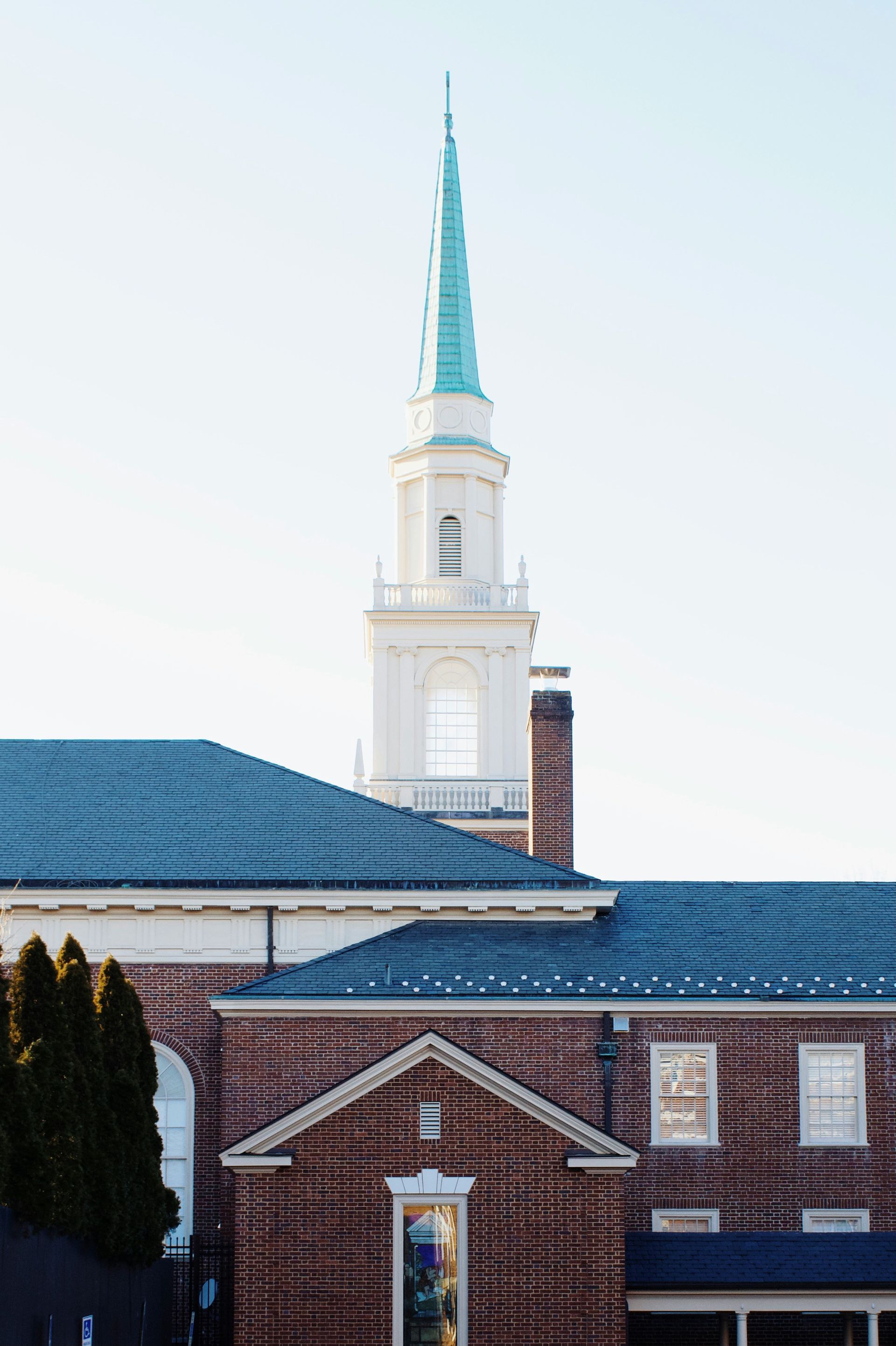 Brick building with a white steeple topped by a teal spire against a light blue sky.
