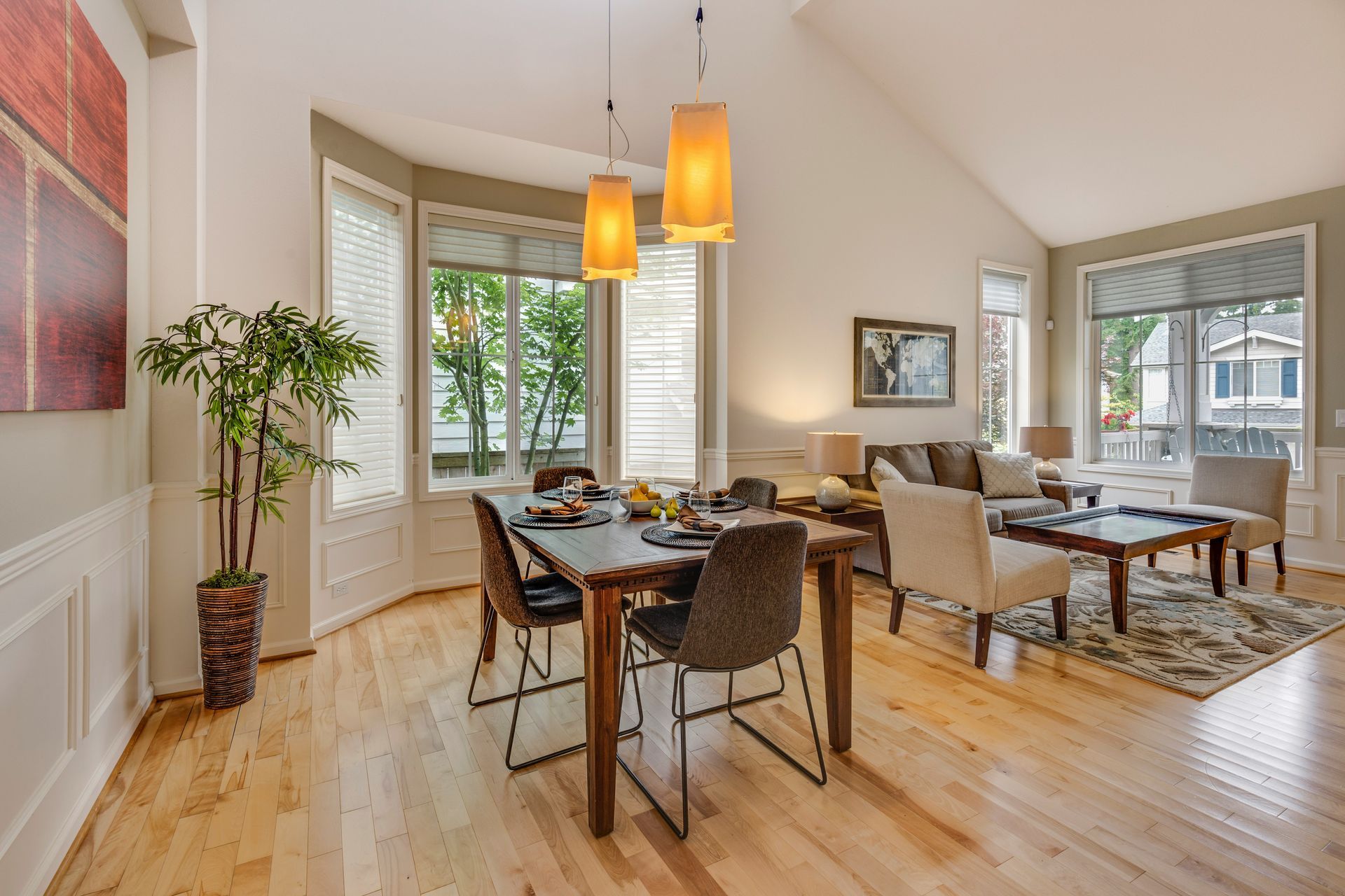 Dining area and living room with wood floors, table, chairs, sofa, windows, and decorative lights.