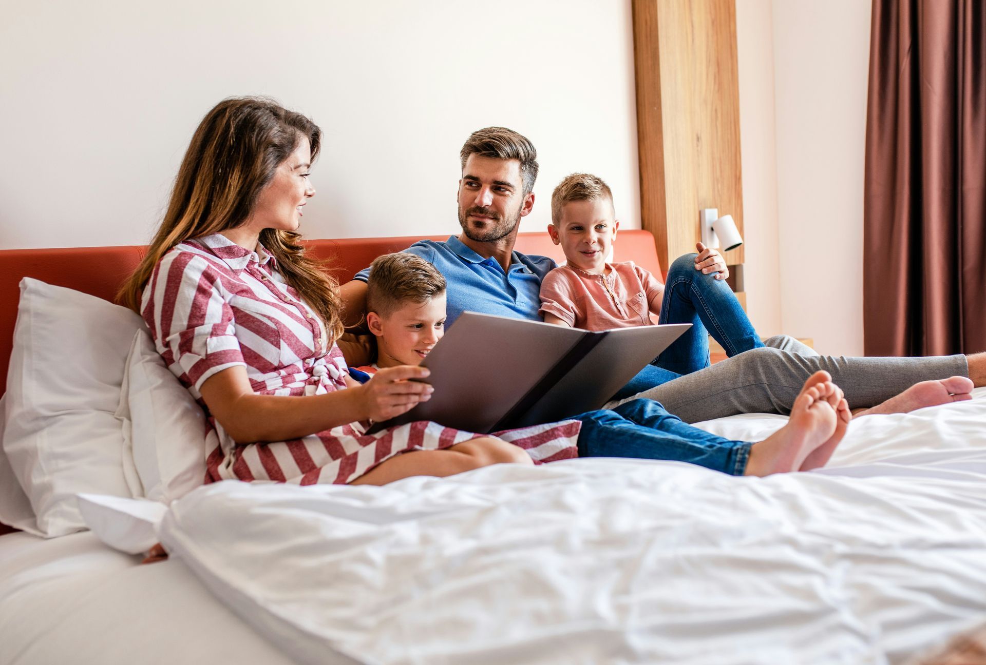 Family reading a book together on a bed in a hotel room.