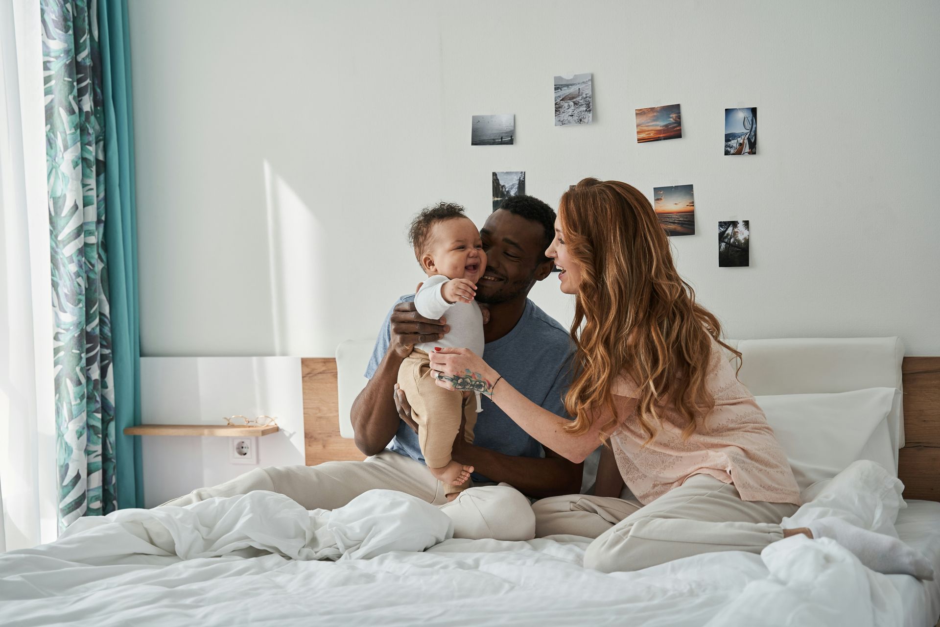 Parents playing with baby on bed; laughing, joyful expressions.