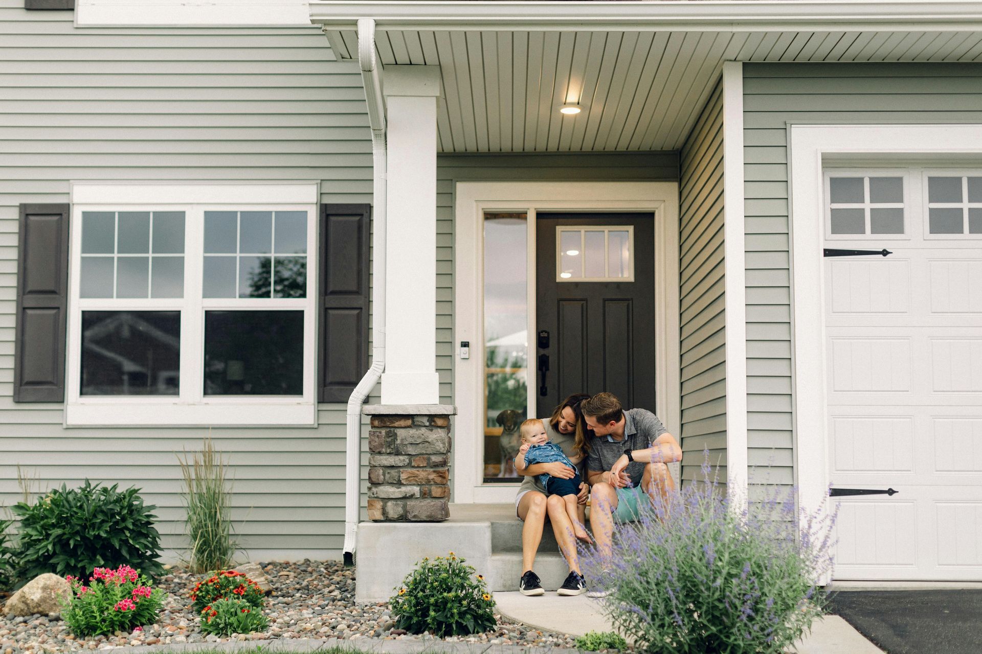 Family sits on porch steps of a house with light blue siding.