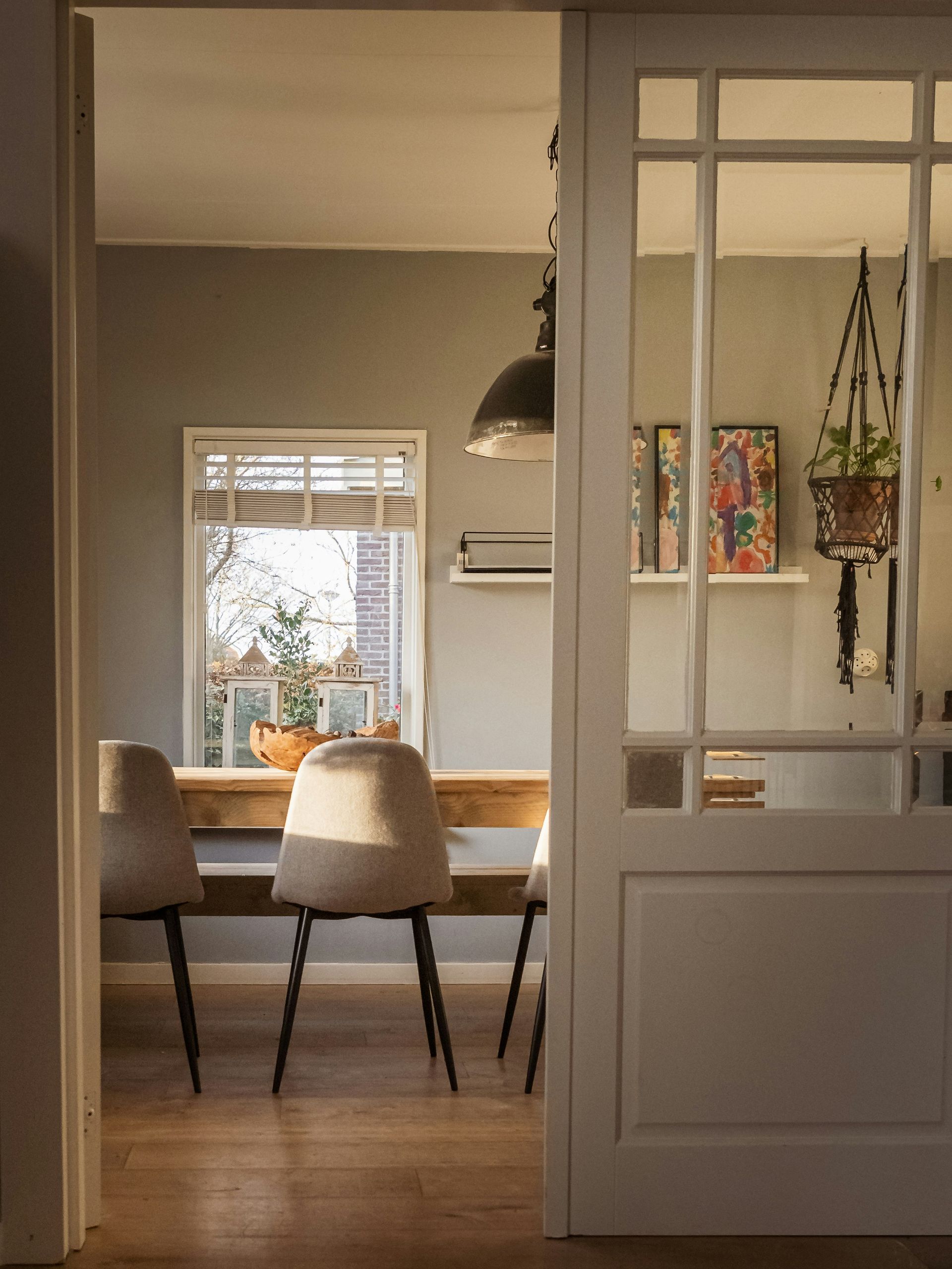 Dining room with wooden table, beige chairs, and glass-paneled door. Sunlight streams through the window.
