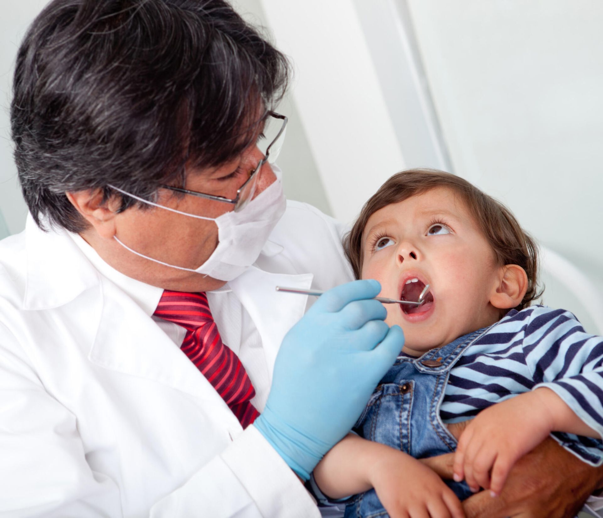 A dentist examines a little boy 's teeth with a mirror
