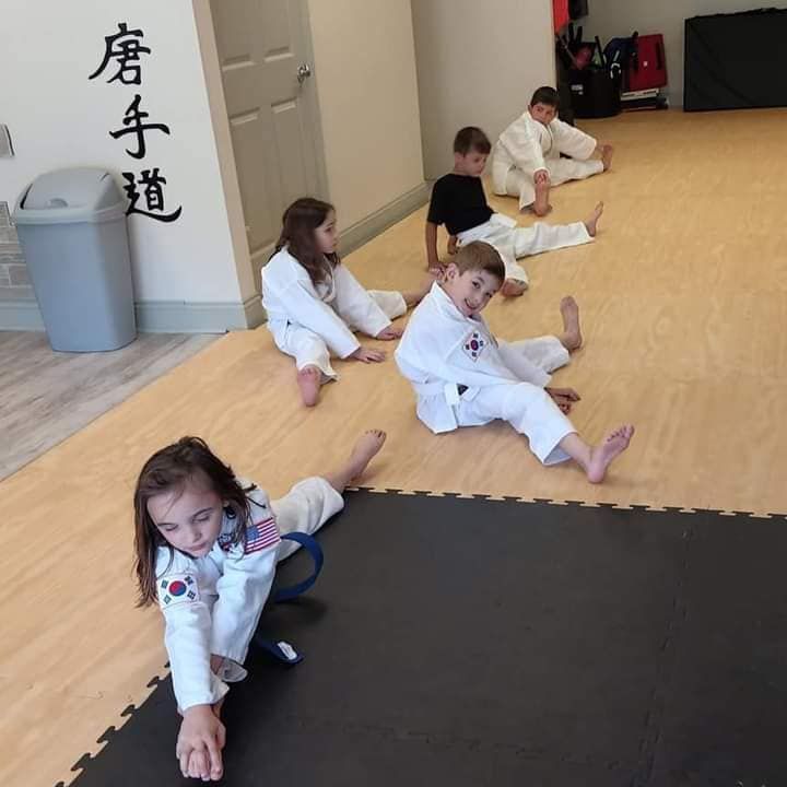 A group of kids are sitting on the floor with chinese writing on the wall behind them