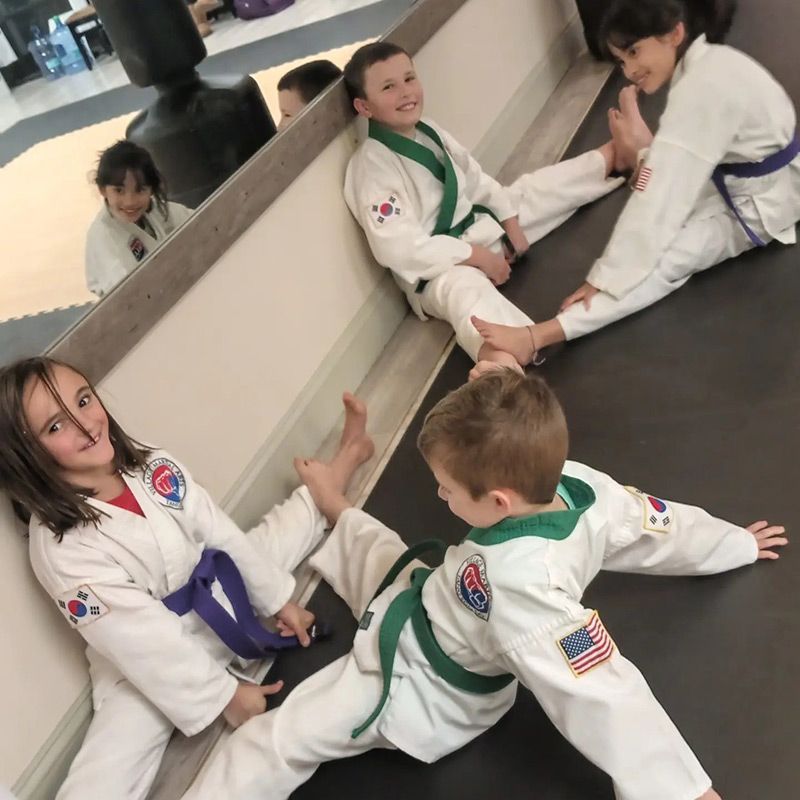 A group of kids in karate uniforms are stretching on a mat