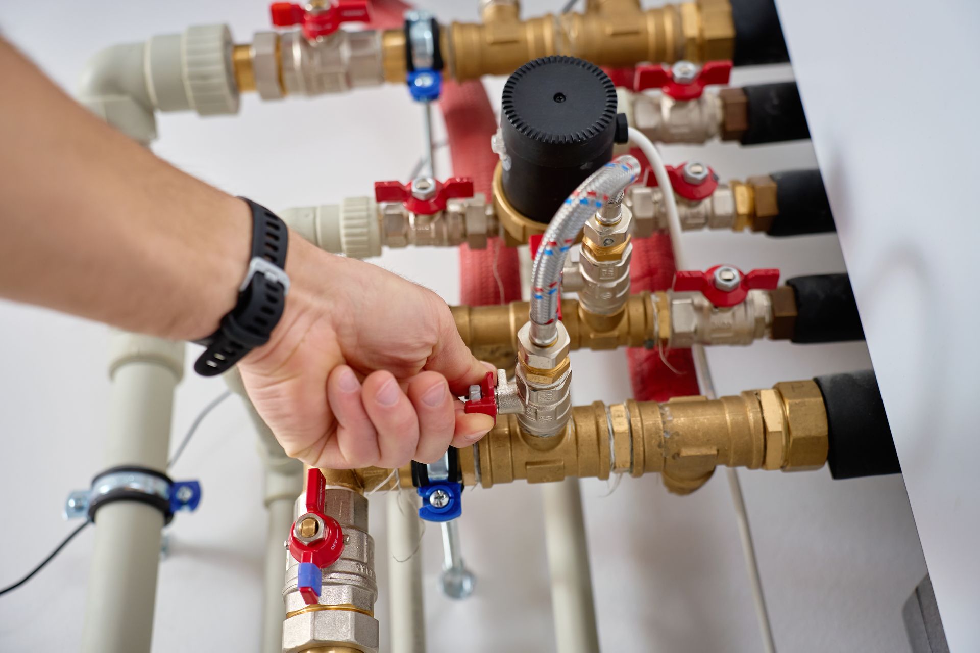 Hand adjusting valves on a complex plumbing manifold with red and blue fittings