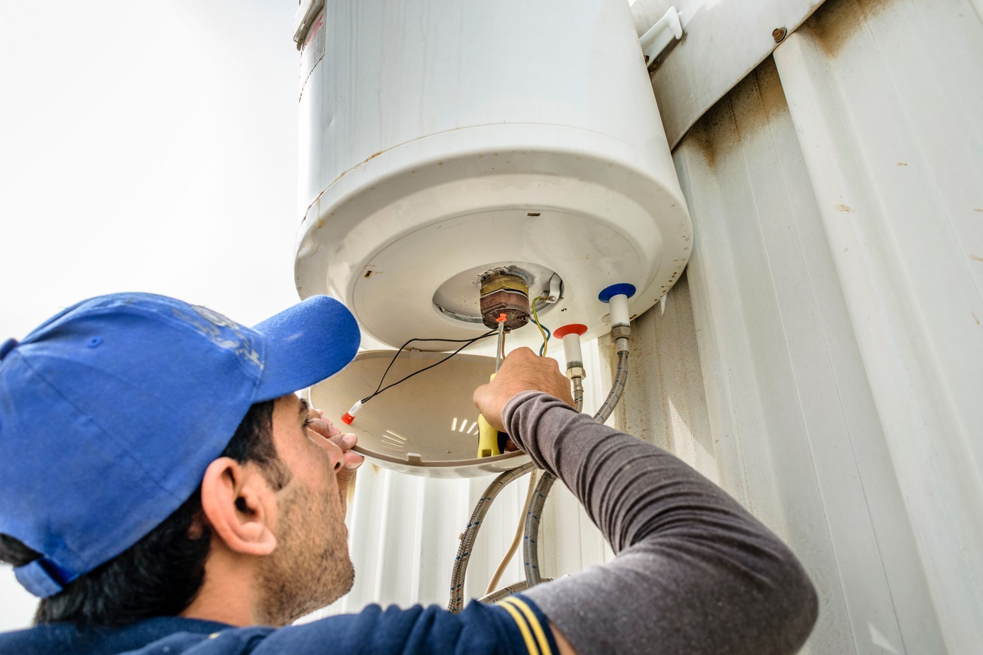 Technician in blue cap inspects wiring on a large white industrial tank