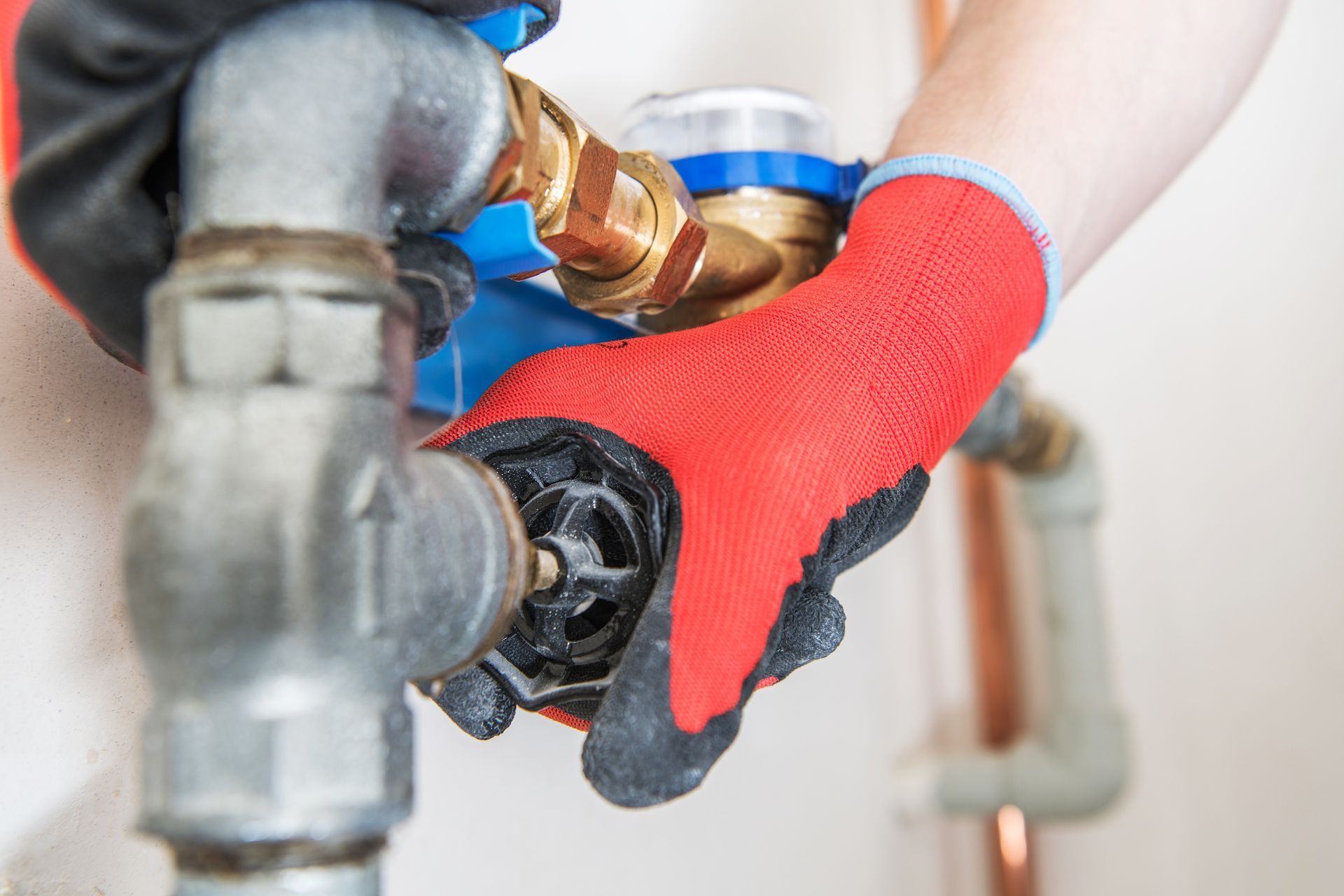 Gloved hands adjusting a faucet valve on plumbing pipes with a wrench