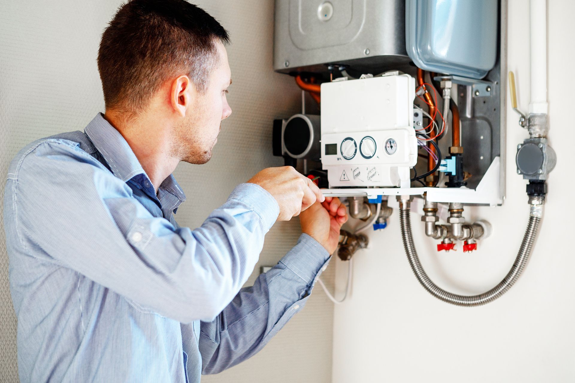 Technician repairing a wall-mounted boiler with exposed pipes and tools in a utility room