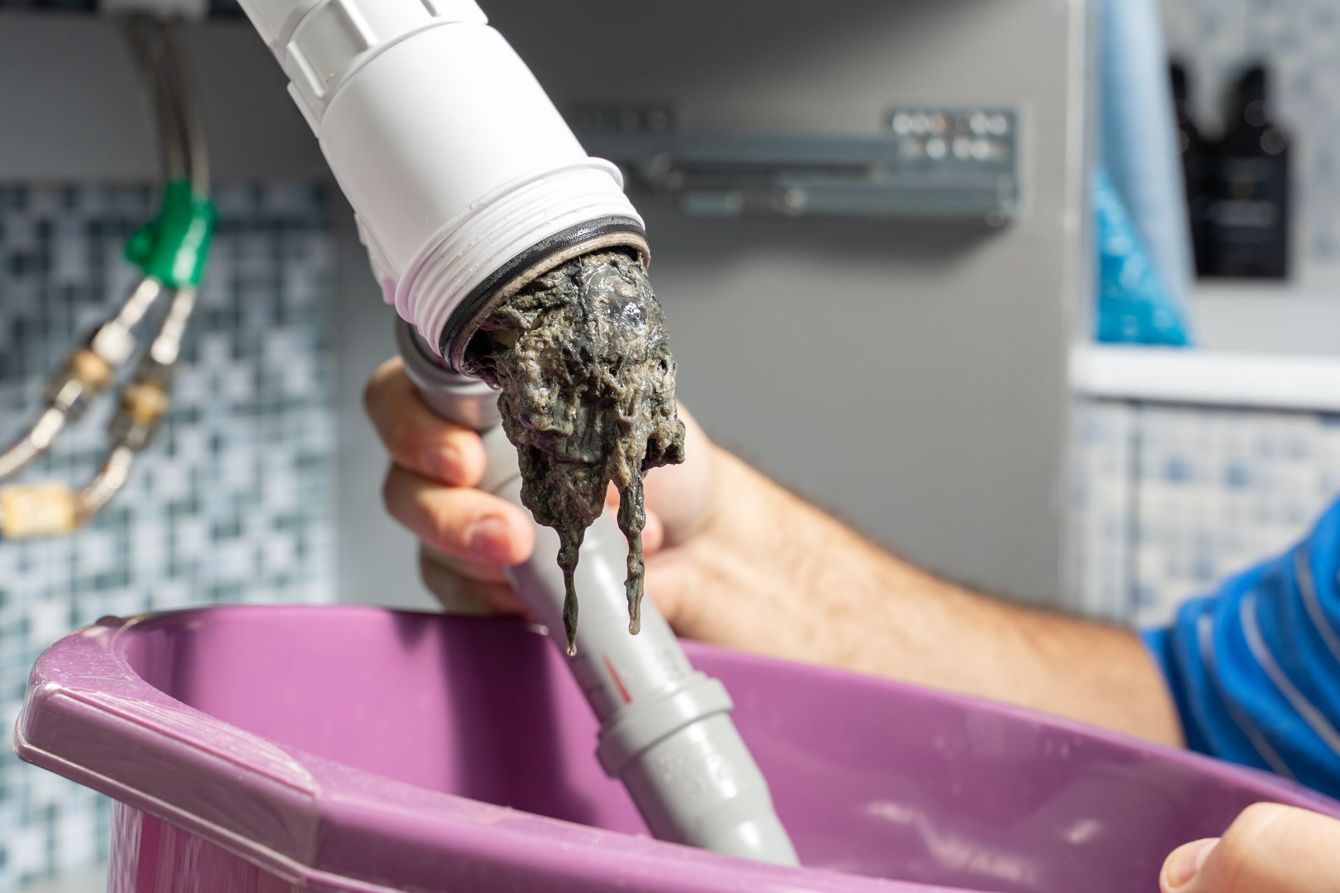 Clogged vacuum hose over a purple tub, with a hand holding the nozzle and debris spilling out