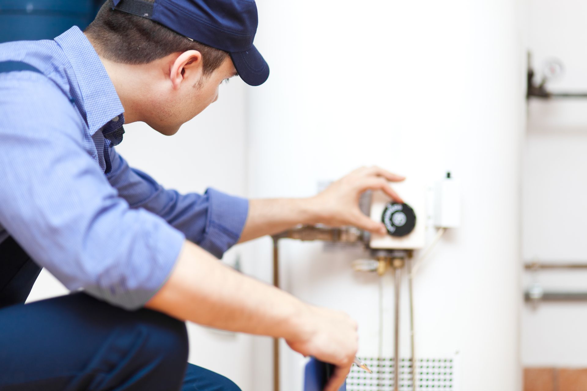 Technician crouching and adjusting a water heater valve with a wrench in a bright utility room