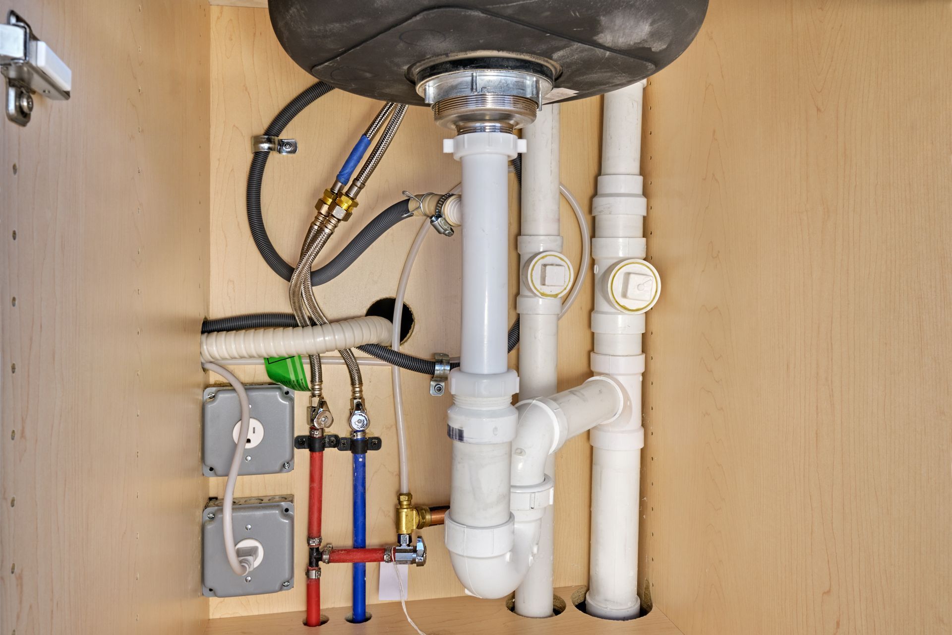 Under-sink plumbing with white PVC pipes, valves, and connections inside a cabinet