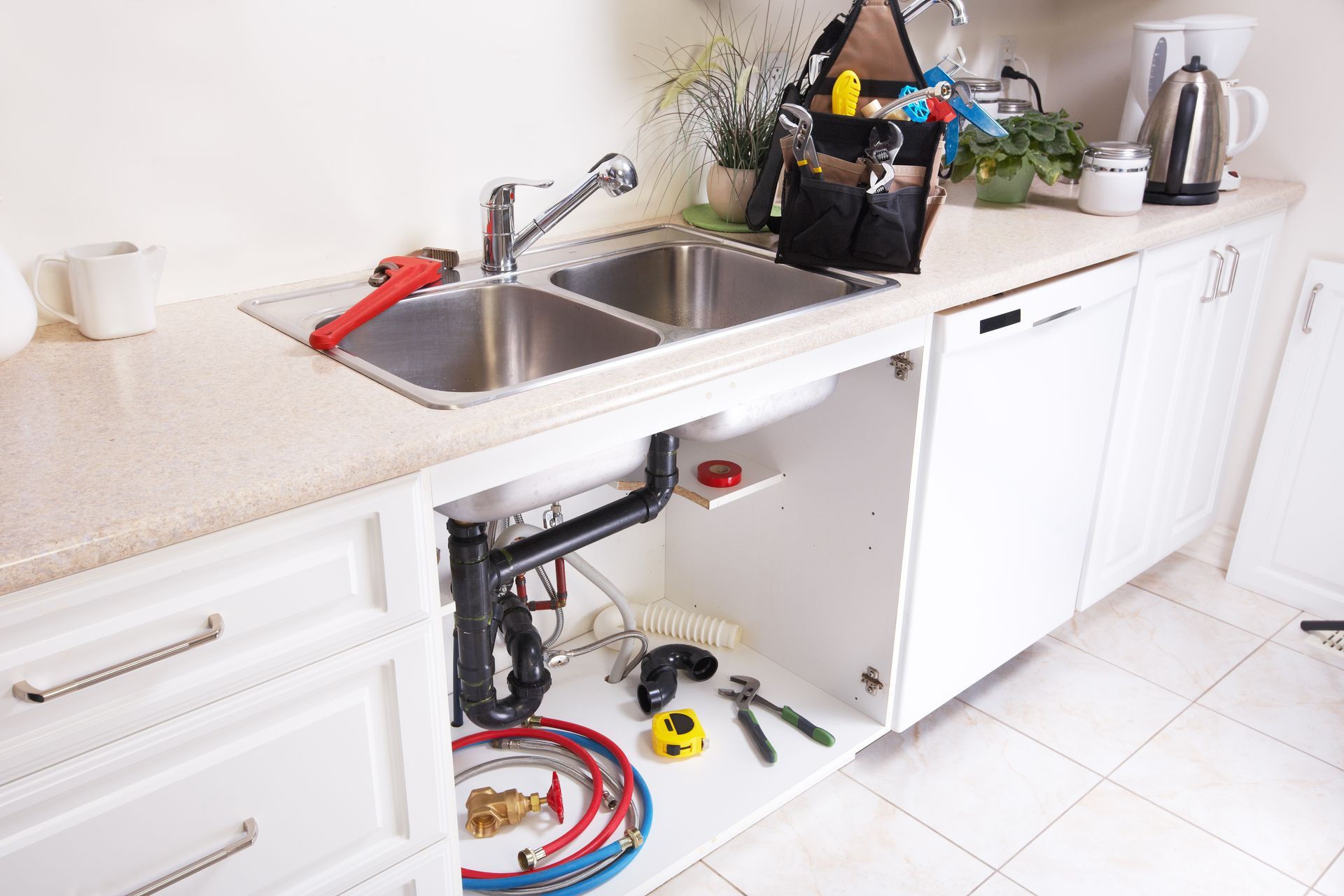 Bright kitchen counter with sink, open cabinet exposing plumbing tools and hoses underneath