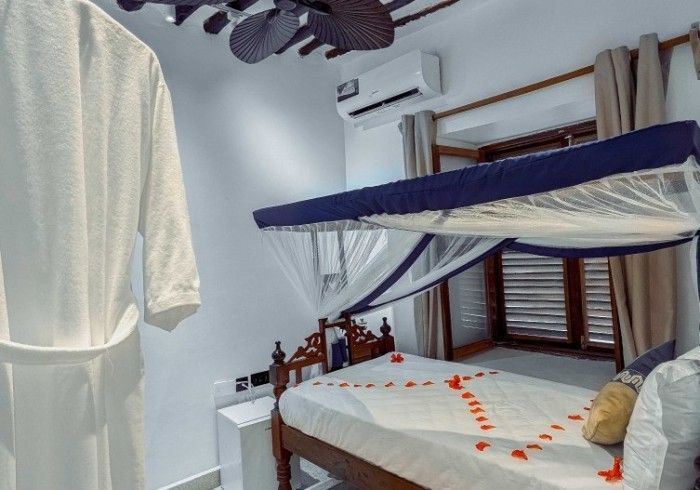 A bedroom with a canopy bed and a white robe hanging from the ceiling.