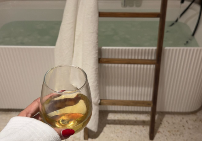 A woman is holding a glass of wine in front of a bathtub