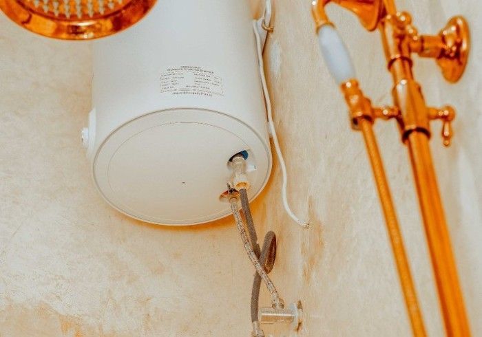 A white water heater is hanging on a wall next to a gold shower head.