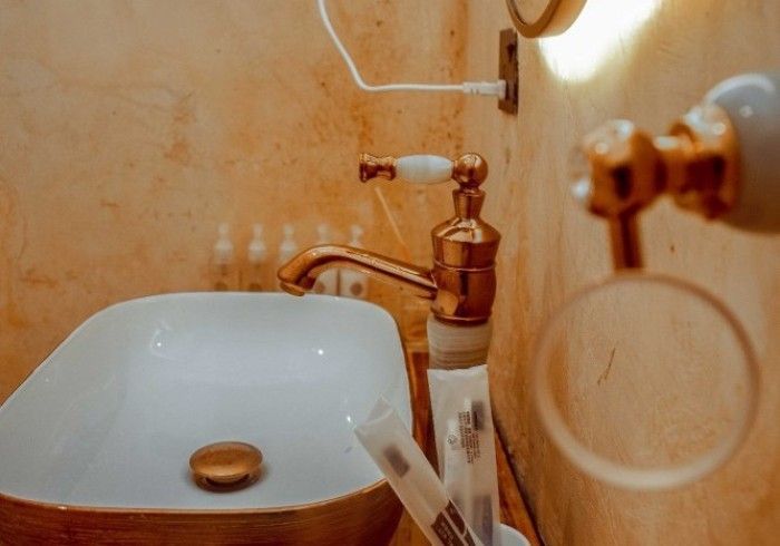 A bathroom with a sink , faucet , mirror and toothbrushes.