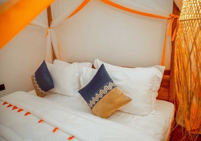 A bed with white sheets and blue and gold pillows under a canopy.