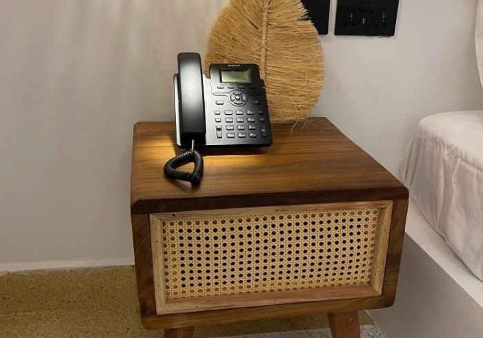 A phone is sitting on a wooden nightstand next to a bed.