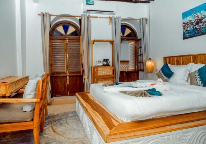 A hotel room with two beds , a desk , chairs and a painting on the wall.