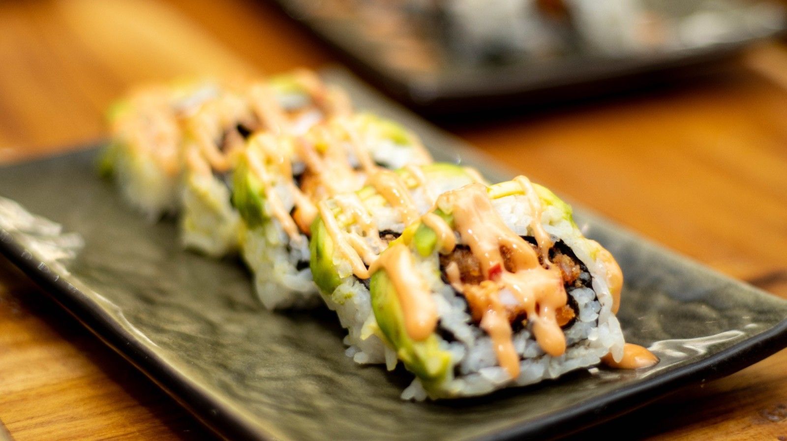 A close up of a sushi roll on a black plate on a wooden table.