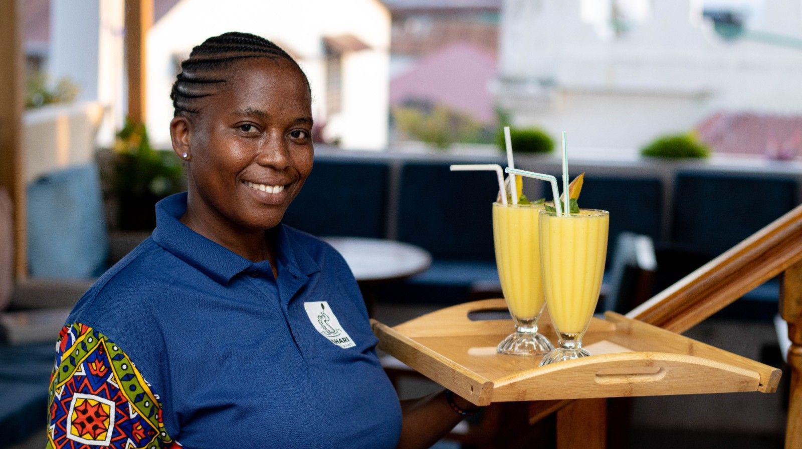 A woman is holding a wooden tray with two drinks on it.