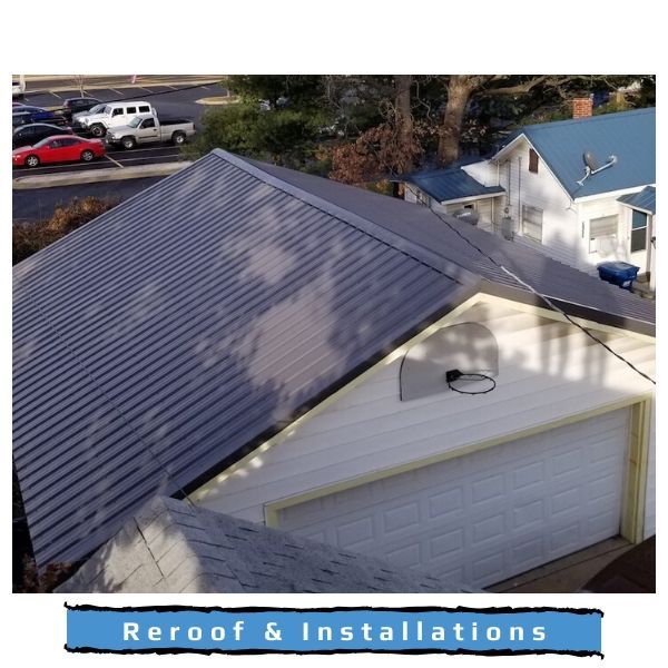 An elevated view of a garage with a newly installed dark metal roof, set against a parking lot and a nearby house.