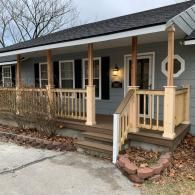 A gray, single-story house with a newly built wooden front porch, railings, and staircase.