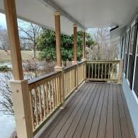 A view of a newly built wooden porch with railings, posts, and brown composite decking overlooking a grassy yard.