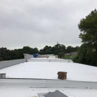 A freshly coated white flat roof under a cloudy sky, with trees visible in the background.