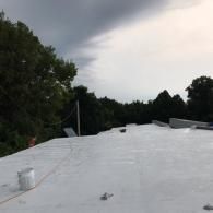 A white, flat roof under a dark, stormy sky with trees in the background.