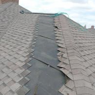A damaged residential roof with missing shingles, exposing the black underlayment along a valley seam.
