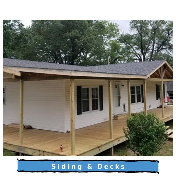 A white house with a newly constructed wooden deck and covered porch, set against a backdrop of green trees.