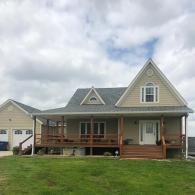 A tan house with a wrap-around porch and an attached garage under a cloudy sky.